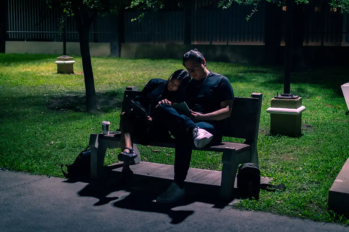 Pareja sentada en una banca de parque por la noche, compartiendo un momento íntimo bajo la luz tenue.