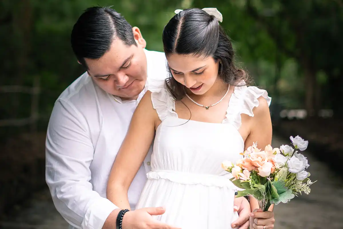 Hombre acariciando el vientre de su pareja mientras ella sonríe con un ramo de flores en las manos.