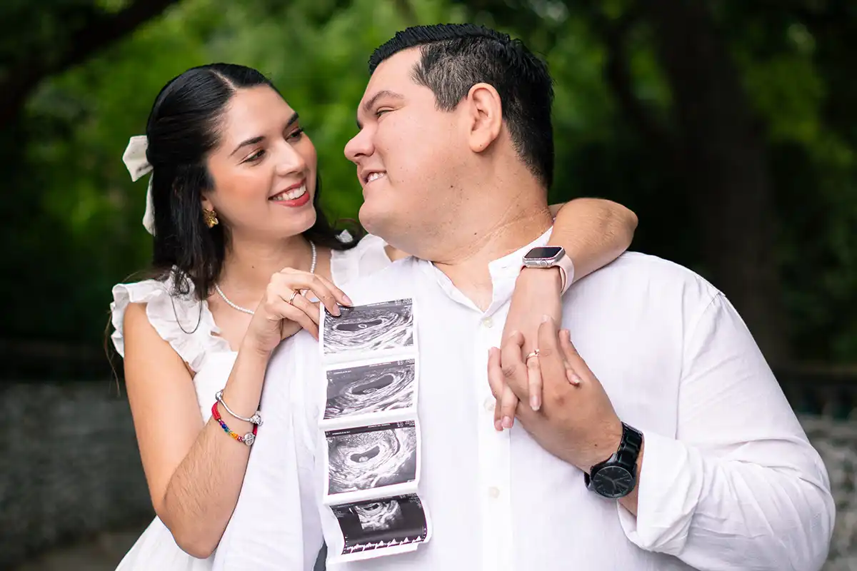 Pareja embarazada sonriendo mientras sostienen juntos un ultrasonido, reflejando alegría y complicidad.